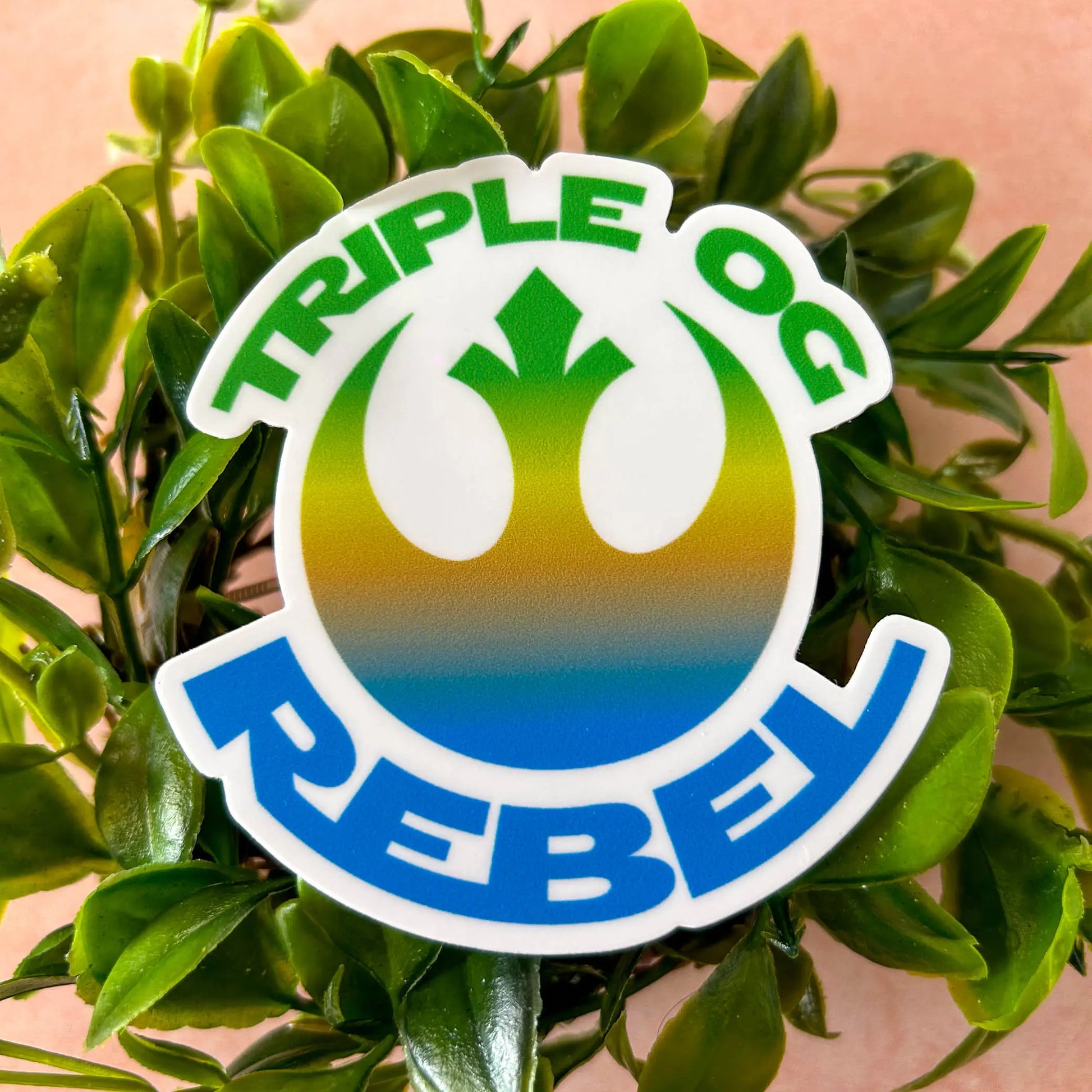 Triple OG Rebel 3" Vinyl Sticker on foliage