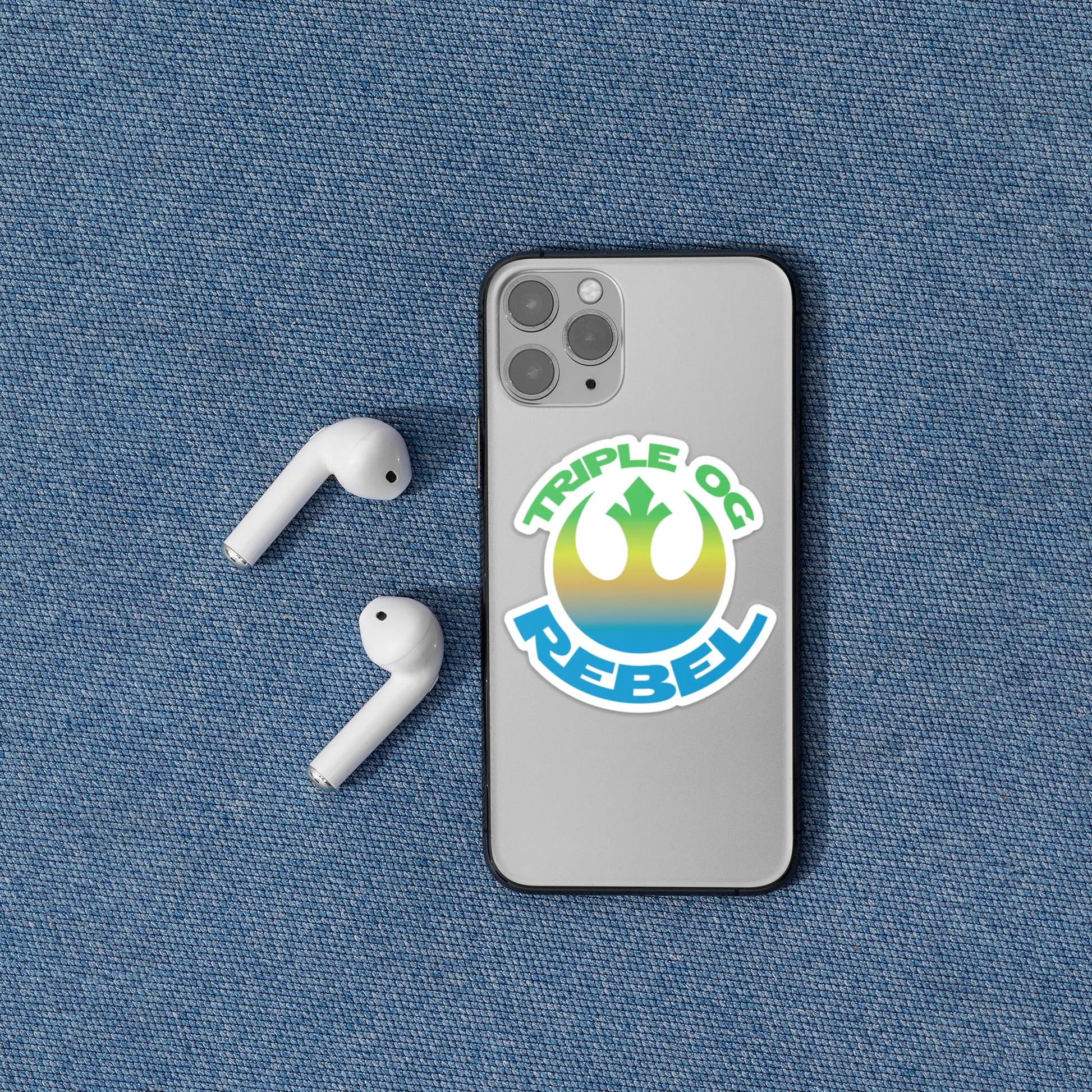 Triple OG Rebel 3" Vinyl Sticker on an iPhone sitting next to AirPods on a denim background