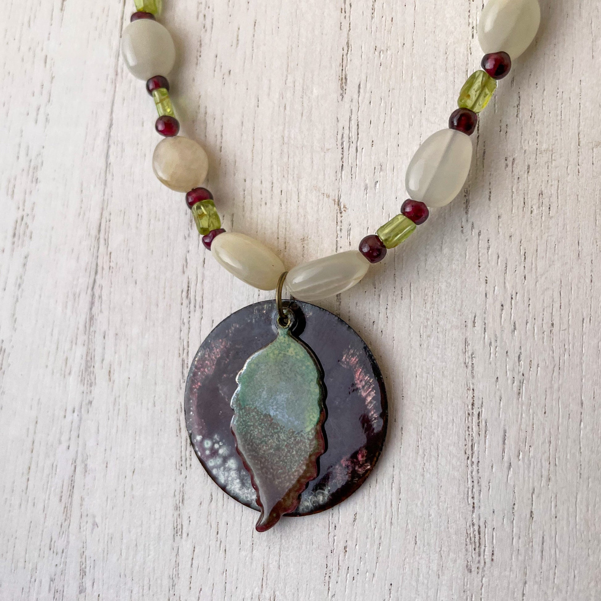 Green Leaf and Burgundy Circle Layered Enamel Pendant Moonstone, Garnet, and Peridot Bead Necklace close up