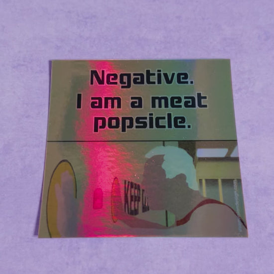 Meat Popsicle Holographic 3" Vinyl Sticker tilted back on a purple background